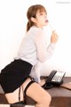 A woman in a white shirt and black skirt sitting at a desk.