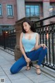 A woman in a blue top and jeans sitting on a railing.