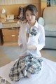 A woman in a white shirt and plaid skirt sitting on a bed.