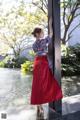 A woman in a red skirt leaning against a pole.