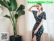 a woman in a black dress standing next to a plant