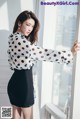 a woman in a polka dot shirt and black skirt leaning against a window