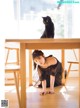 A woman in a black dress sitting at a table with a black cat.