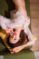 A woman laying on a green couch with her hands on her face.