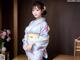 A woman in a blue kimono standing in front of a table.