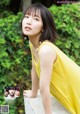 A woman in a yellow dress leaning against a wall.