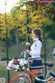 A woman standing next to a bike with a basket of flowers.