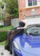 A woman in a black dress sitting on top of a blue car.