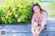 A woman sitting on a wooden bench in front of flowers.