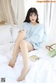 A woman sitting on a bed in a blue sweater.