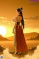 A woman in a long dress standing in front of a sunset.