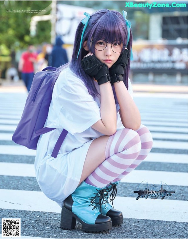 A woman with purple hair and glasses sitting on the ground.