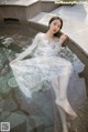 A woman in a white dress sitting in a pool of water.