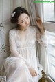 A woman in a white dress sitting on a window sill.