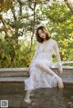 A woman in a white dress sitting on a stone ledge.