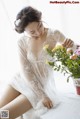 A woman sitting on a bed next to a vase of flowers.