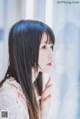 A woman with long black hair standing in front of a window.