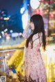 A woman in a pink dress standing on a balcony at night.