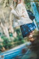 A woman in a plaid skirt and a beige jacket is walking down a path.