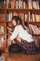 A woman sitting on the floor in front of a bookshelf.