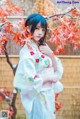 A woman in a kimono standing in front of a tree.