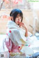 A woman in a kimono sitting on a wooden floor.