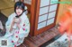 A woman in a kimono sitting on a wooden floor holding a cup.