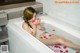 A woman laying in a bathtub with rose petals on the floor.