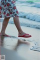 A woman walking on the beach wearing red flip flops.