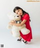 A woman in a red dress holding a white teddy bear.