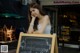 A woman sitting at a table in front of a blackboard.