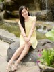 A woman in a yellow dress sitting on a rock by a waterfall.