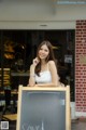 A woman standing in front of a coffee shop holding a sign.