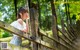 A woman leaning against a wooden fence in the woods.