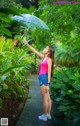 A woman holding an umbrella in the middle of a lush green forest.