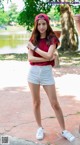 A woman in a red shirt and white shorts posing for a picture.