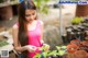 A woman in a pink tank top is looking at a plant.