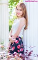 A woman leaning against a white wall with flowers in her skirt.