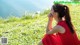 A woman in a red dress sitting on the grass by the water.