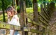 A woman leaning against a wooden fence in the woods.