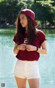 A woman in white shorts and a maroon shirt is standing by the water.