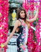 A woman in a floral dress standing in front of pink flowers.