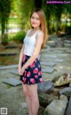 A woman in a white tank top and floral skirt posing for a picture.