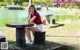 A woman sitting on top of a wooden table next to a lake.