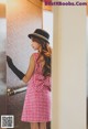 A woman in a pink dress and black hat standing in an elevator.