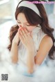 A woman in a white dress sitting on a bed with her hands on her face.