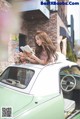 A woman laying on top of a green car reading a book.