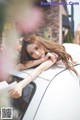 A woman leaning on the hood of a white car.