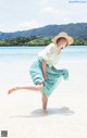 A woman in a blue dress and straw hat on the beach.