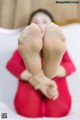 A woman in a red dress is sitting on a bed with her feet up.